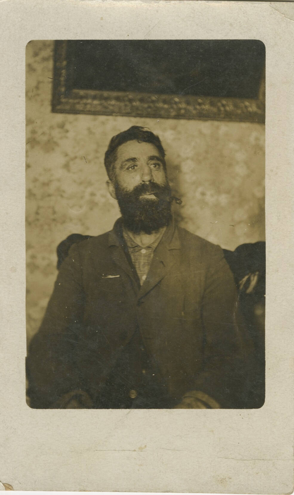 Historic photograph of a man sitting in chair, wearing a suit jacket with dark hair and beard.